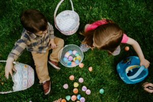 Girl in green jacket playing with white and pink plastic balls on green grass field during Easter